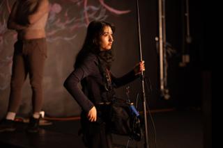 Boom operator holding the microphone pole steady on set, the mural glowing on the wall behind