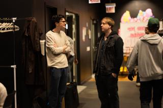 Two crew members talking in the corridor beside a rack of wardrobe, others passing behind them