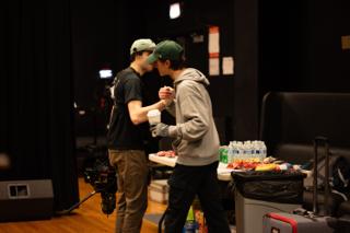 Two crew members leaning in close beside the craft table, one handing over a coffee cup
