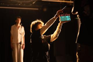 Crew member holding a clapperboard overhead as the actor waits in the background