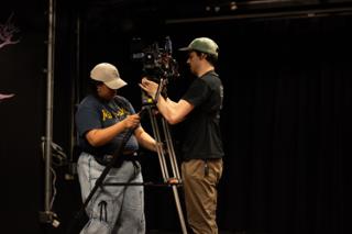 Two camera crew building the camera onto its tripod on the darkened stage