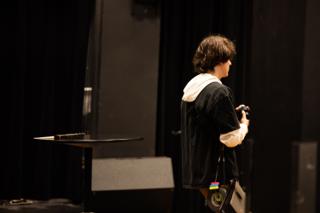 Lone crew member watching from the edge of the darkened stage, headphones slung at their side