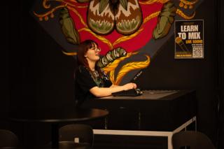 Sound mixer at the desk beneath a large painted mural, smiling mid-conversation