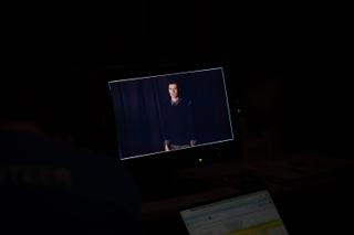 Monitor on a dark desk showing the actor mid-take, a laptop glowing below it