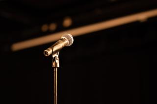 Microphone on a stand lit from above against a dark stage