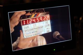 Camera monitor showing a clapperboard held in front of the lens, the film's title written across it