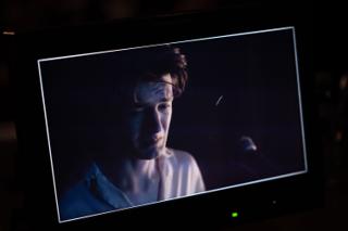 Camera monitor showing the actor in a dim, blue-lit close-up