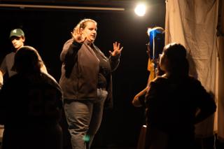 Crew member gesturing with both hands while giving direction to the team on a darkened stage