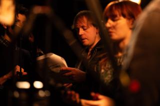 Crew member reading from a script page, framed between out-of-focus colleagues and equipment