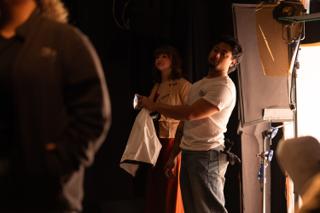 Crew member adjusting an actor's costume beside a lighting unit