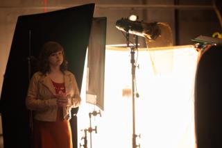 Actor standing beside a lit backdrop surrounded by lighting stands and diffusion frames