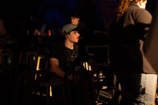 Crew member in a backwards cap seated among the tables, watching the set