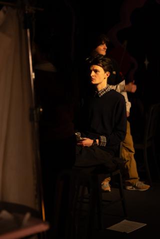 Actor seated on a stool between takes, waiting at the edge of the set