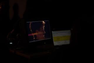 Two screens glowing in a dark corner, one showing the actor mid-take and the other a shot log