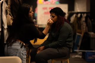 Makeup artist applying makeup to a seated crew member in the dressing area