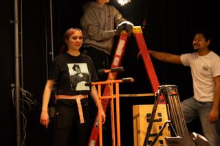 Crew steadying a stepladder and equipment cart while a colleague works above