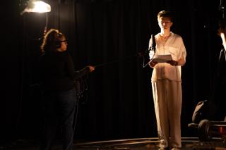Boom operator holding a microphone toward the actor, who reads from a script on the lit stage