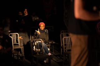 Person seated among rows of chairs in the venue, smiling and raising a peace sign