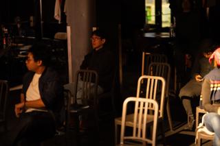 Crew seated among rows of chairs in the dimly lit venue between setups