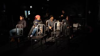 Crew seated among rows of chairs in the darkened house, watching the stage