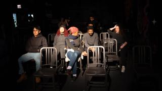 Crew sitting together in the rows of chairs during a break in filming