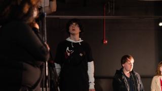 Performer looking upward under the stage lights, crew watching from either side