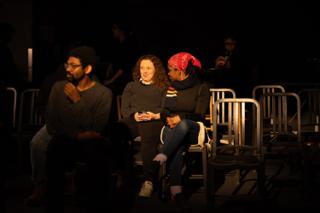 Three crew members sitting together in the rows of chairs, watching a take