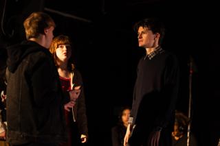 Three actors playing a scene by candlelight on the darkened stage