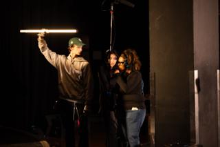 Crew member holding a tube light aloft beside the camera and sound team