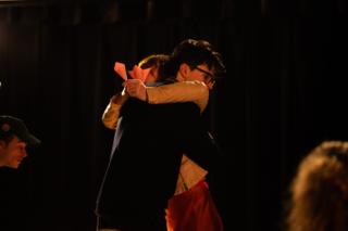 Two actors embracing during a scene, a lit candle between them
