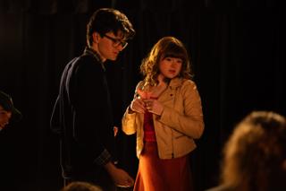 Two actors sharing a candle in a scene, lit only by its flame