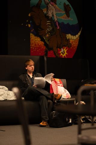 Actor reading through script pages on a green room sofa beneath a painted mural