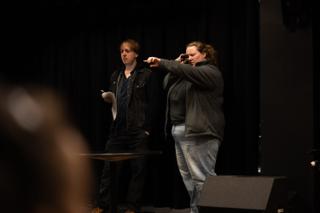 Two crew members blocking a scene on the darkened stage, script pages in hand